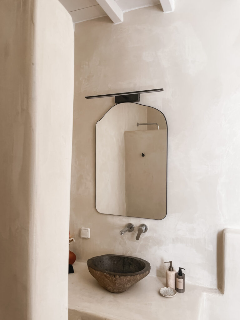 cement bathroom with rock sink, irregular shaped mirror and high ceilings